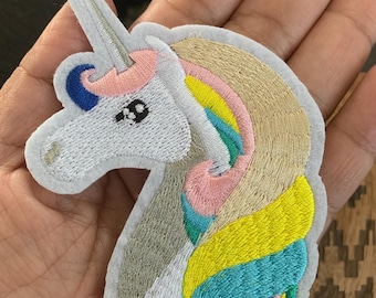 May include: White unicorn embroidered patch with a rainbow mane. The mane is made of yellow, blue, green, and pink thread. The unicorn has a pink horn and blue eyes.