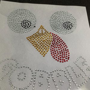 May include: A white fabric sheet featuring a turkey face design made of rhinestones. The eyes are silver with black pupils, the beak is gold, and the wattle is red. The word "GOBBLE" is spelled out in silver rhinestones below.