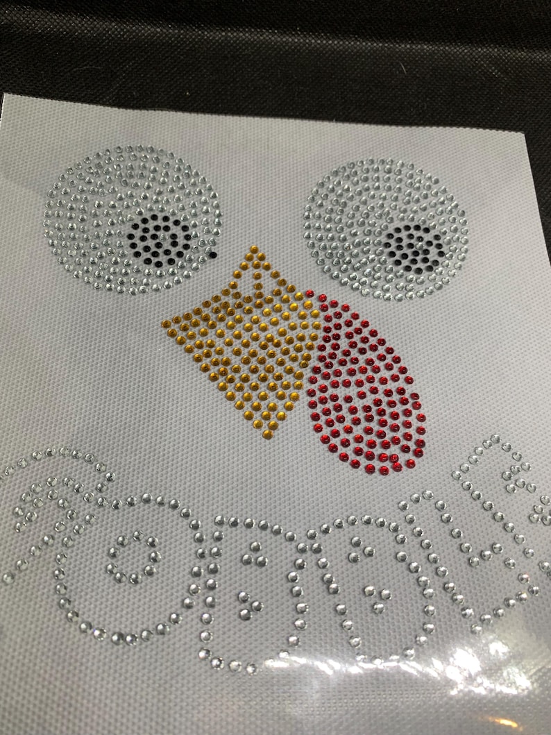 May include: A white fabric sheet featuring a turkey face design made of rhinestones. The eyes are silver with black pupils, the beak is gold, and the wattle is red. The word "GOBBLE" is spelled out in silver rhinestones below.