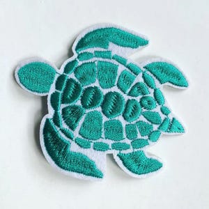 May include: A teal blue embroidered iron-on patch of a sea turtle with a white background.