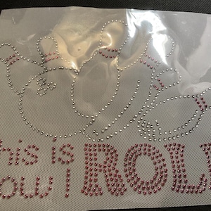 May include: A rhinestone design on a mesh backing. The design features a bowling pin and ball motif, with the words "This is how I ROLL" spelled out in pink rhinestones. The bowling pin and ball are outlined in silver rhinestones.