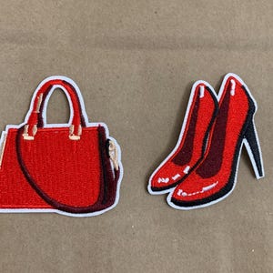 May include: Embroidered patches featuring a red handbag with a handle and a pair of red high heels with black heels. The patches have a white border and are set against a neutral background.