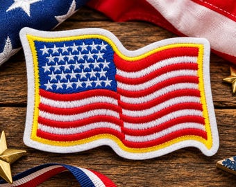 May include: A rectangular embroidered patch featuring the American flag with a wavy design. The patch has a blue canton with white stars, red and white stripes, and a thick yellow border, all outlined in white felt on a textured surface.