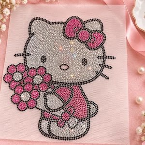 May include: A diamond painting craft kit featuring a Hello Kitty character design. The image is composed of small, sparkling rhinestones in shades of silver, pink, and black, depicting the character holding a bouquet of flowers on a light pink canvas.