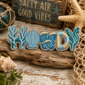 May include: An embroidered patch featuring the word HOWDY, where each letter is creatively formed by coastal elements. The H is made of blue coral, the O is a blue seashell, the W is blue ocean waves, the D is a blue and gold life ring, and the Y is teal coral.