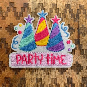 May include: Embroidered patch featuring three party hats in blue, yellow, and purple with star toppers. The patch includes the phrase "PARTY TIME" in pink lettering, perfect for adding to clothing or accessories.