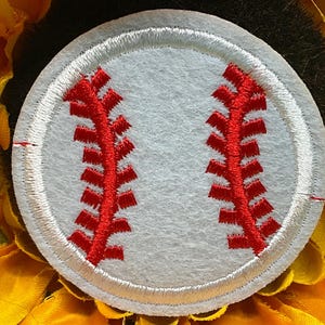 May include: A white baseball patch with red stitching, set against a backdrop of yellow and green. The baseball design is circular, with detailed red stitching mimicking the seams of a baseball. The background features a sunflower.
