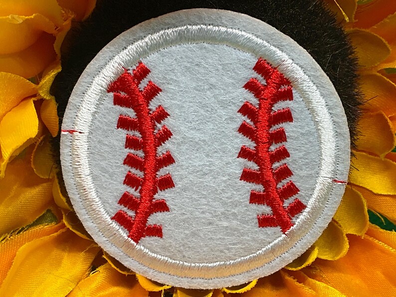 May include: A white baseball patch with red stitching, set against a backdrop of yellow and green. The baseball design is circular, with detailed red stitching mimicking the seams of a baseball. The background features a sunflower.