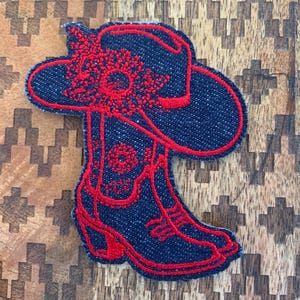 May include: A denim patch with red embroidery of a cowboy hat and boots. The hat has a flower design on the brim.
