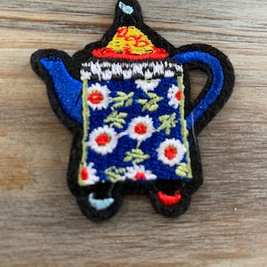 May include: A blue teapot with a white and red floral pattern and a yellow lid. The teapot has a black outline and a blue handle.