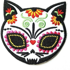 May include: Embroidered iron-on patch featuring a black and white cat skull with pink and yellow floral details. The cat's eyes are black with yellow accents.