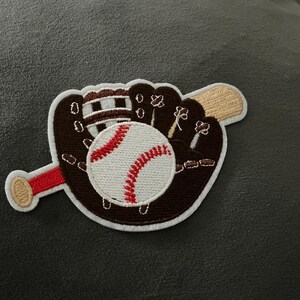 May include: Embroidered patch featuring a baseball and glove design. The baseball is white with red stitching, and the glove is brown with white accents. A tan baseball bat is also included in the design.