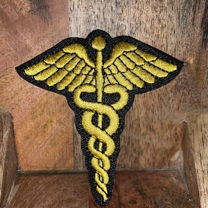 May include: A gold embroidered medical symbol with wings, also known as the Rod of Asclepius, on a black background.