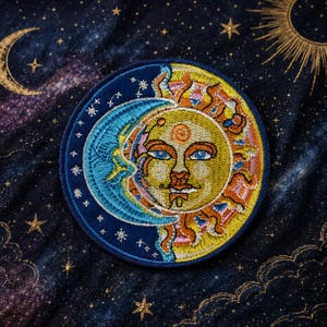 May include: A circular embroidered patch featuring a split design of a yellow sun with a human face and a blue crescent moon. The sun has orange rays and blue eyes, while the moon is surrounded by small white stars on a dark blue background.
