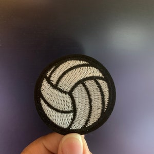 May include: A white volleyball embroidered patch with black stitching on a black background.
