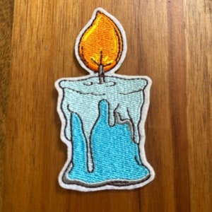 May include: A blue and white embroidered iron-on patch of a melting candle with a yellow flame.