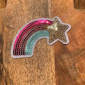 May include: A rainbow-colored sequin patch with a gold star. The rainbow is made of pink, red, and turquoise sequins. The star is made of gold sequins.