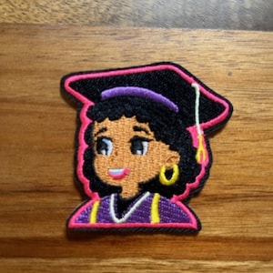 May include: Embroidered patch featuring a cartoon graduate with dark skin, wearing a black graduation cap with a pink outline and a gold tassel. The patch has a pink and purple border, and the graduate is wearing a purple graduation gown with yellow accents.