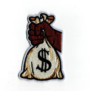 May include: Embroidered patch of a brown hand holding a beige money bag with a black dollar sign.