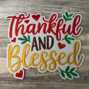 May include: Embroidered patch with the words "Thankful and Blessed" in red, brown, and yellow. The patch features heart and leaf accents, and is on a white background.