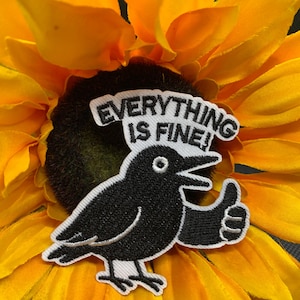 May include: A black crow patch with the text "EVERYTHING IS FINE!" giving a thumbs up. The patch is on a yellow sunflower with a dark brown center.