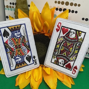 May include: Two rectangular embroidered patches featuring playing card designs. The left patch depicts the King of Spades with a sword, while the right patch shows the Queen of Hearts. Both patches have white borders and detailed thread work.