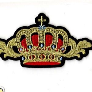 May include: A gold embroidered crown with red and blue accents. The crown has a pointed top and is surrounded by a black fabric.