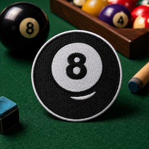 May include: A circular embroidered patch featuring a black background with a white center circle containing a black number eight. The patch has a white border and a small white curved line at the bottom, mimicking the design of a billiard ball.