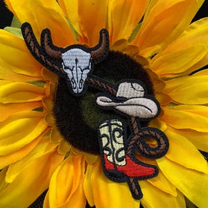 May include: Embroidered patches featuring a steer skull, cowboy hat, and cowboy boot with a rope design. The patches are in shades of brown, beige, red, and black, set against a yellow sunflower.