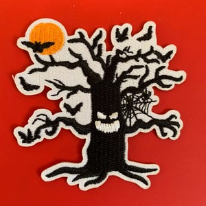 May include: A Halloween-themed patch featuring a spooky black tree with a carved face, bats, and a spiderweb. An orange moon is visible in the upper left corner. The patch is on a red background.