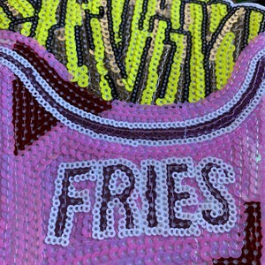 May include: A pink and white sequined patch with the word "FRIES" in white sequins and a yellow and black sequined image of french fries.
