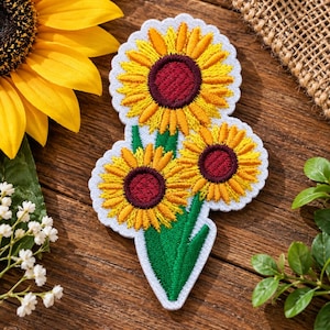 May include: An embroidered patch featuring three sunflowers with bright yellow petals and dark maroon centers. The design includes green stems and leaves, all outlined with a white scalloped border, creating a distinct floral motif.