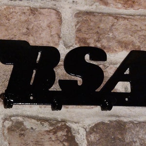May include: Black metal key holder with the word "BSA" and a stylized wing design. The key holder has five hooks.