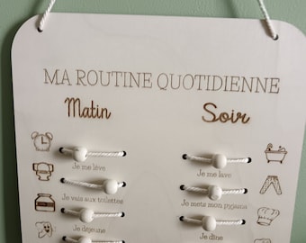 May include: A white wooden board with the text "MA ROUTINE QUOTIDIENNE" at the top. The board is divided into two sections, "Matin" and "Soir". Each section has a list of activities with corresponding icons, such as a clock, a toothbrush, and a bed. The activities are written in French.