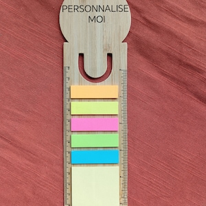 Peut inclure: Une règle en bois avec une découpe en forme de smiley et le texte "PERSONNALISE MOI" en haut. La règle est munie d'un ensemble de notes autocollantes colorées.