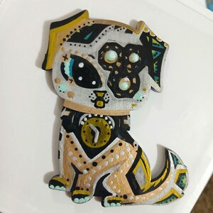 May include: A hand-painted wooden dog figurine with a unique design. The dog features a mix of colors, including gold, black, silver, and teal. The dog has a clock-like design on its chest and intricate patterns throughout its body.