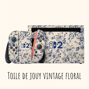 Könnte beinhalten: Eine Nintendo Switch-Konsole und Controller mit einem cremefarbenen und blauen floralen Toile de Jouy-Design. Die Controller haben schwarze Knöpfe und eine korallenfarbene Schiene. Der Text "Nintendo Switch" und "2" ist auf der Konsole und den Controllern sichtbar.