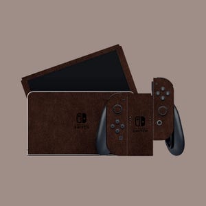 Pode incluir: Um conjunto de skins castanhas texturizadas para uma consola Nintendo Switch, incluindo a consola principal, dois comandos Joy-Con e o ecrã. A skin tem um aspeto semelhante a couro e cobre toda a consola e os comandos. O logótipo Nintendo Switch é visível.