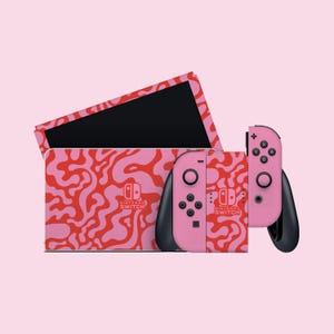 May include: Pink Nintendo Switch console and two pink Joy-Con controllers with a red and pink abstract pattern. The console has the Nintendo Switch logo on the front.