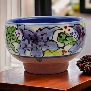 May include: A small, blue and white ceramic bowl with a floral design. The bowl has a wide rim and a rounded base.