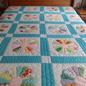 Peut inclure: Une courtepointe faite à la main avec un motif floral. La courtepointe présente un fond bleu clair et blanc avec des motifs floraux circulaires colorés. La courtepointe est sur un cadre de lit en bois.