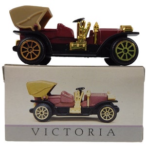 May include: A red and black toy car with a tan top and gold accents. The car is labeled "VICTORIA" on the box.