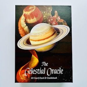 May include: A boxed set of "The Celestial Oracle" cards and guidebook. The cover shows a planet with rings, an orange peel, and grapes. The text reads "The Celestial Oracle" and "44 Card Deck & Guidebook" on a dark background.