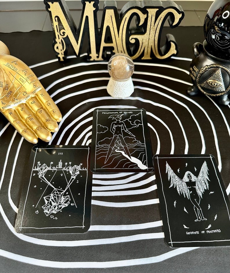 May include: Three black tarot cards with white illustrations on a black and white circular background. The cards are "Philosopher of Knives", "III", and "Goddess of Feathers".
