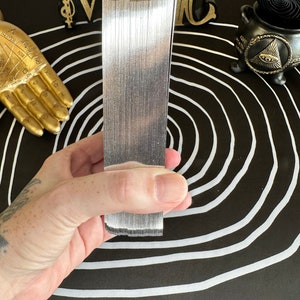 May include: A stack of silver playing cards, held in a hand, against a black and white background with a circle pattern.