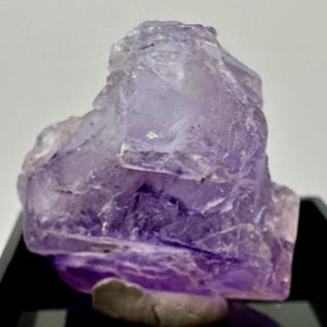 May include: A large, purple fluorite crystal with a rough, textured surface. The crystal has a deep purple color with some lighter areas. It is a natural mineral specimen.