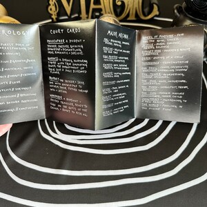 May include: A set of black and silver tarot cards with gold lettering. The cards are folded to show the titles "Court Cards", "Major Arcana", and "Wheel of Fortune". The cards feature descriptions of each card's meaning.
