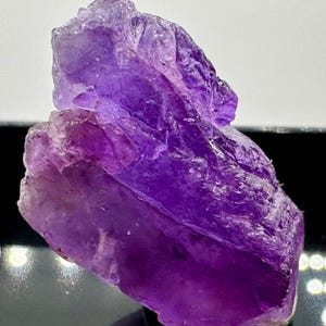 May include: A large, deep purple amethyst crystal with a rough, natural texture. The crystal has a pointed tip and a flat base.