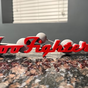 May include: A 3D printed red and white sign that reads "Foo Fighters".