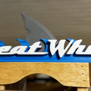 May include: A blue and white wooden sign with the text "Great White" in white letters. A gray shark fin is above the text.